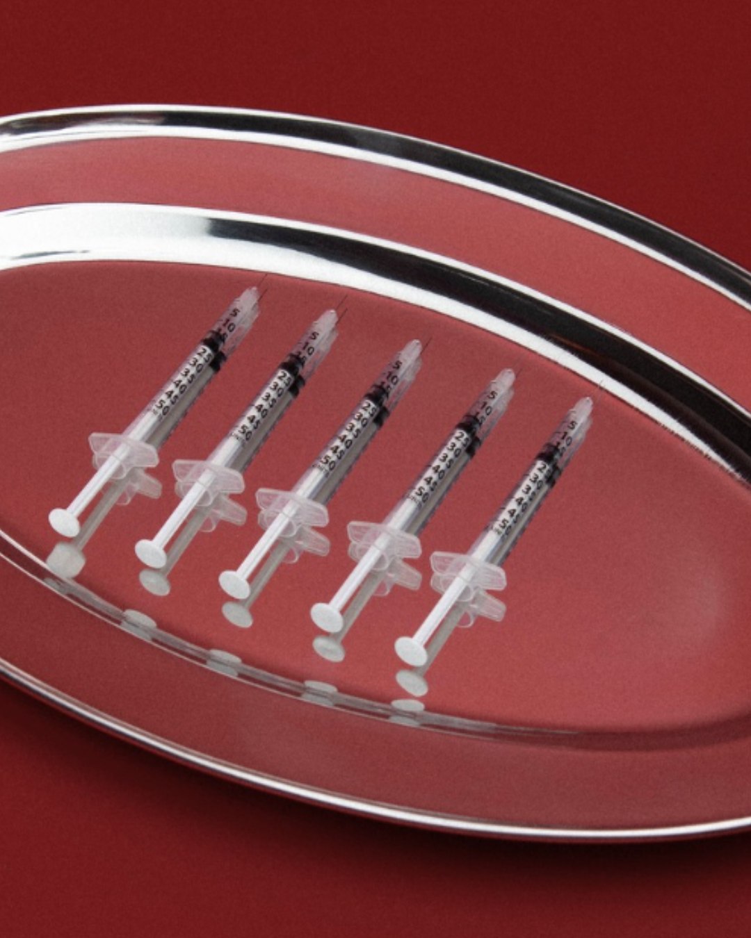 A polished red treatment tray arranged with five aesthetic syringes